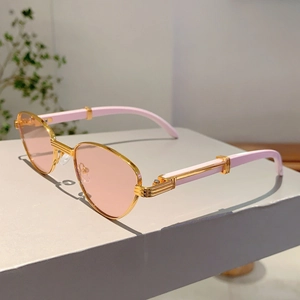 Detail view of pink tinted lenses and golden metal frame with decorative C-hinge element