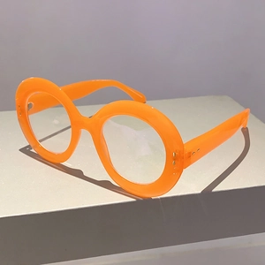 Detail view of bright orange round oversized glasses frames on a gray geometric stand