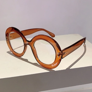Detail of round oversized amber eyeglasses frame with metallic rivets on a pedestal