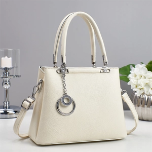 Elegant off-white lychee texture handbag with silver ring charm on a minimalist desk