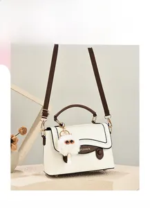 Détail d'un sac à main crème en similicuir avec surpiqûres noires et pendentif peluche