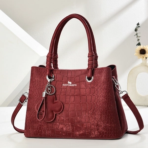 Close-up of deep red crocodile embossed leather handbag with metal charms and straps