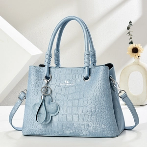 Detail of light blue crocodile embossed handbag with metal logo and floral charm