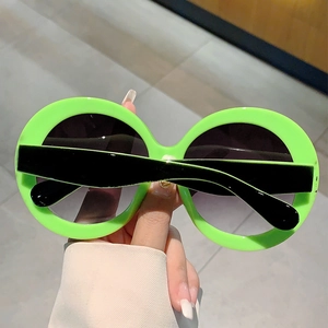 Detail of neon green oversized round sunglasses featuring dark grey gradient lenses
