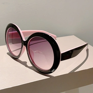 Detail of round oversized sunglasses with black frame, pink interior, and purple gradient lenses