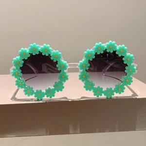 Close-up of circular resin sunglasses with 3D turquoise daisy flowers and gradient lenses