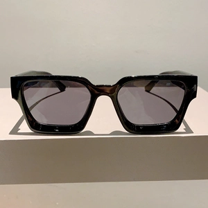 Lunettes de soleil carrées noires classiques avec verres foncés sur un support beige épuré