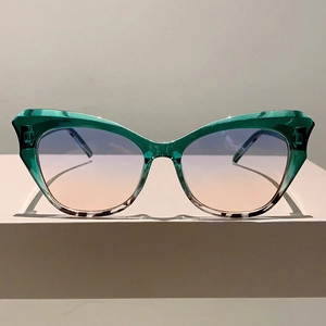 Macro detail of green cat-eye sunglasses with gradient lenses on a minimalist stand