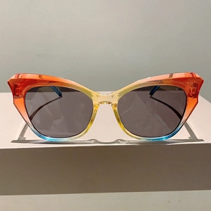 Detail of cat-eye sunglasses featuring a unique red-yellow-blue gradient frame with gray lenses