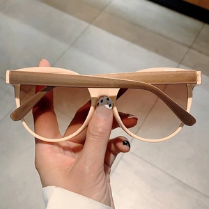 Detail view of large cat-eye sunglasses with light pink frames and gradient brown lenses