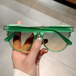 Close-up of green transparent cat eye sunglasses with brown gradient lenses in hand