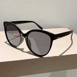 Detail view of oversized black cat-eye sunglasses with dark grey lenses on white podium
