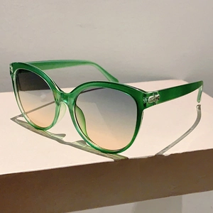 Detail view of emerald green cat-eye sunglasses featuring blue and orange gradient lenses