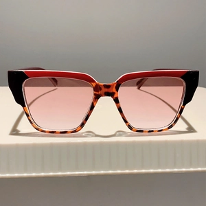 Detail of square oversized sunglasses with red frames and pink gradient lenses