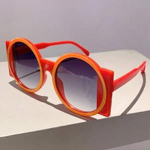 Detail view of bold red and orange contrast round sunglasses with geometric frame wings