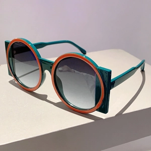 Detail view of bold round sunglasses with contrasting green and orange frames on a pedestal