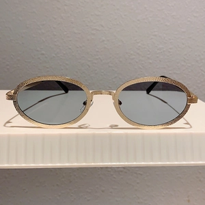 Close-up of vintage oval gold metal sunglasses with unique hammered texture and dark gray lenses