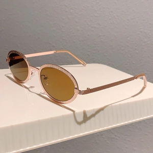 Detail of retro oval sunglasses with rose gold textured frame and tinted brown lenses