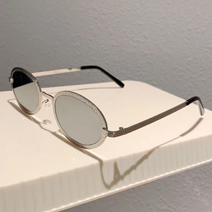 Detailed macro view of silver oval metal frame with textured finish and grey lenses