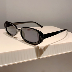 Dettaglio di occhiali da sole ovali vintage con montatura nera e lenti grigie su supporto