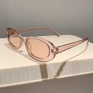 Dettaglio degli occhiali da sole ovali vintage con montatura rosa champagne e lenti marroni