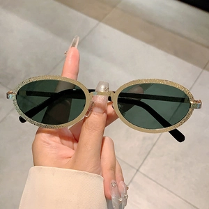 Retro oval sunglasses with matte gold glitter frame and dark lenses held by hand