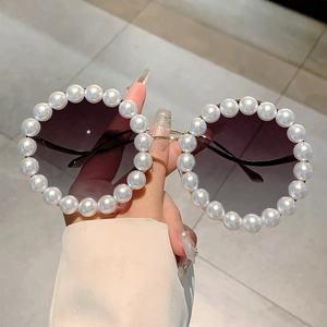 Detail einer runden Sonnenbrille mit handgesetzten weißen Perlen und Goldrahmen
