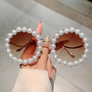 Detail einer runden Sonnenbrille mit Goldrahmen und großen Perlenverzierungen
