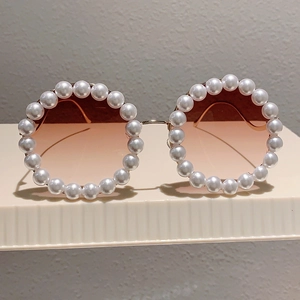 Details einer runden Sonnenbrille mit weißen Perlenverzierung und goldenen Metallbügeln