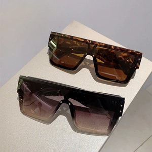 Detail view of square oversized sunglasses with silver metal rivets on neutral background
