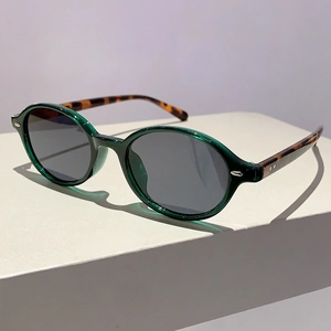 Detail view of oval sunglasses featuring dark green frames and tortoiseshell temples