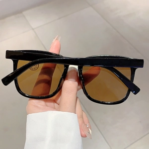 Detail einer quadratischen schwarzen Sonnenbrille mit braunen Gläsern in der Hand