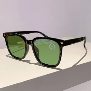 Detail der quadratischen schwarzen Sonnenbrille mit grünen Kristallgläsern und Goldakzenten