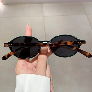Oval vintage sunglasses with dark lenses and tortoise shell patterns held by hand