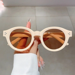 Close-up of retro cream round frame sunglasses with metal rivet accents and brown lenses