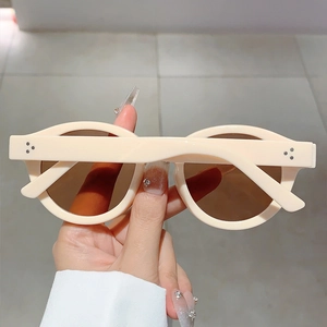 Detail of cream oval sunglasses featuring silver rivets and brown tinted lenses