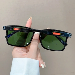 Détail de lunettes de soleil carrées noires avec verres vert foncé et accents orange