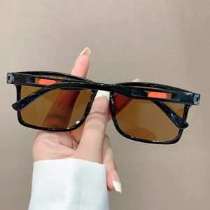 Détail de lunettes de soleil noires carrées avec verres bruns et accents de branches orange