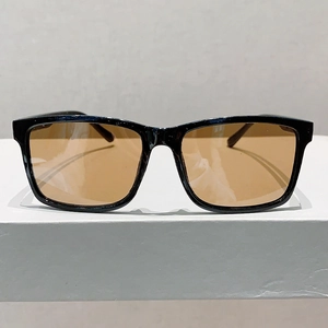 Vue de face de lunettes de soleil noires carrées avec des verres ambrés sur socle