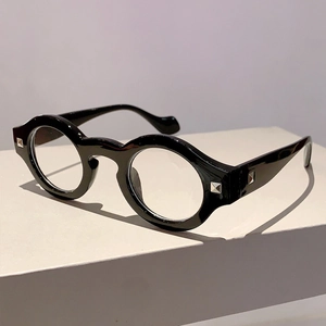 Detail view of bold round black frames with silver rivet accents on a minimal pedestal