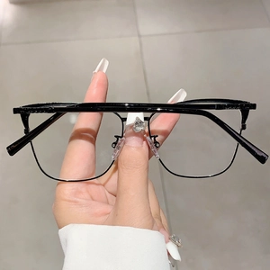 Vue détaillée de lunettes œil-de-chat en métal noir tenues à la main avec verres anti-lumière