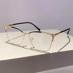 Détail de lunettes œil-de-chat avec monture en métal doré, accents noirs et cristaux