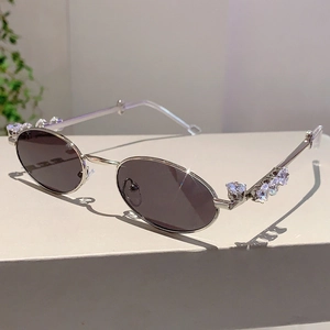 Dettaglio degli occhiali da sole ovali argento con aste decorate con cristalli e lenti scure