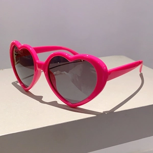 Detailansicht der herzförmigen hellrosa Sonnenbrille mit dunkelgrauen Gläsern auf weiß