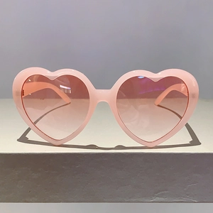 Detailansicht der pinkfarbenen Herz-Sonnenbrille mit Verlaufsgläsern auf grauem Grund