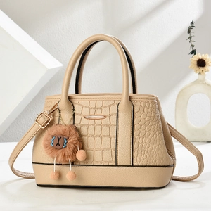 Detail der beigen Handtasche mit Krokoprägung, Metallstab und süßem Plüsch-Anhänger
