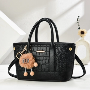 Detail der schwarzen Handtasche mit Krokodilprägung, Metallleiste und Plüschtier-Anhänger