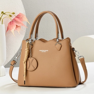 Elegant tan lychee leather handbag with adjustable strap and decorative charm for women