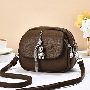 Detail view of brown lychee leather bag featuring three zipper layers and bear charm