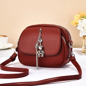 Detail of burgundy leather shoulder bag with silver bear pendant and zipped sections